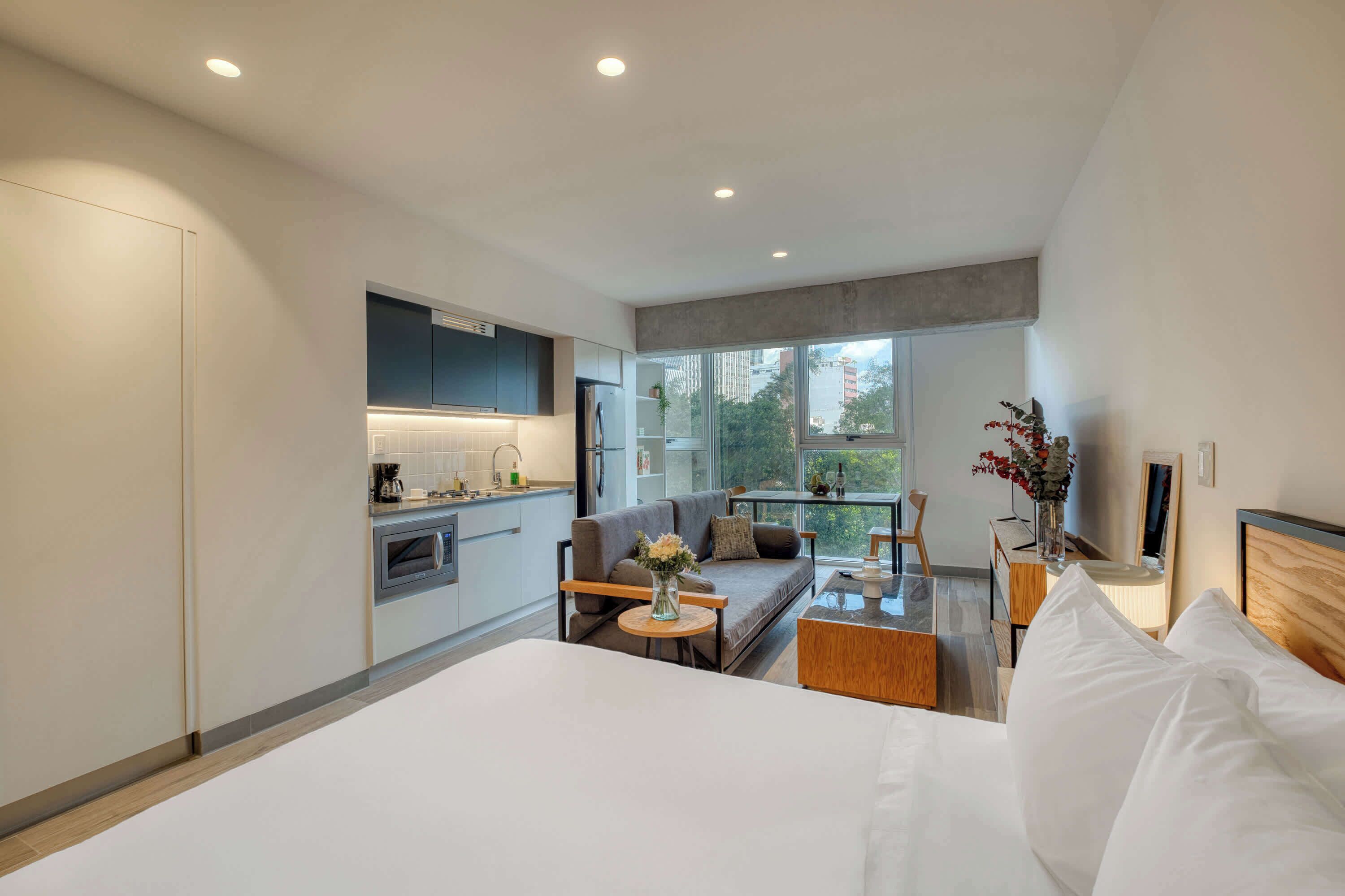 Habitació d'hotel moderna amb cuina sencera, sofà, taula de menjador i llit gran.