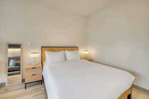 Ein Hotelzimmer mit einem großen Bett, zwei Nachttischen mit Lampen, einem Holzkopfstück und einem Spiegel an der linken Wand.