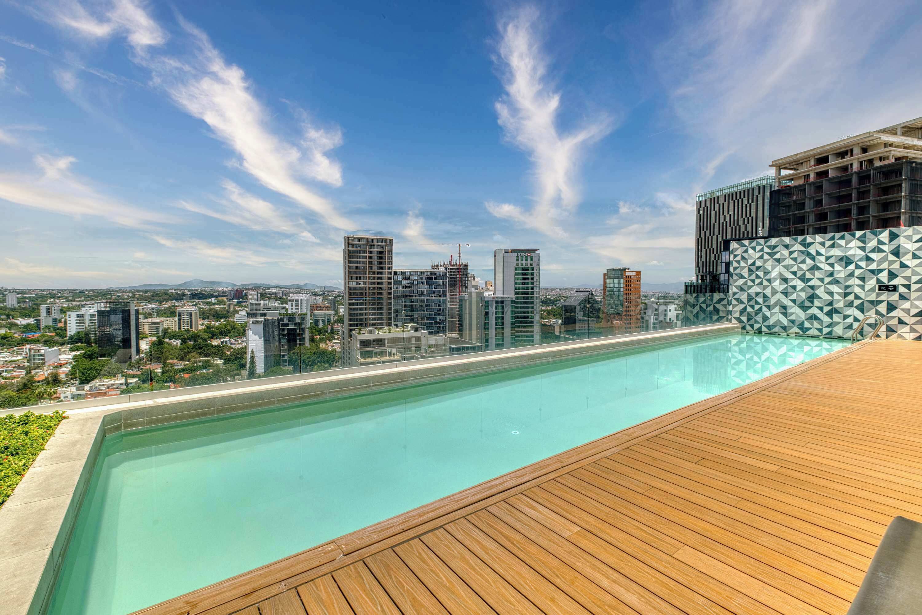 A rooftop pool with a clear view of the city skyline, including several high-rise buildings and a construction crane.