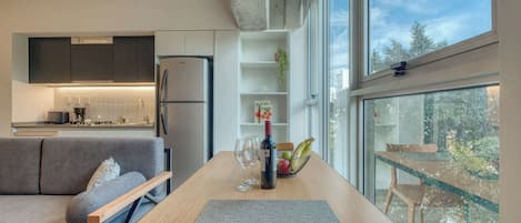 A modern kitchen with a built-in refrigerator, a dining area with a wooden table, and a view of the outdoors through large windows.
