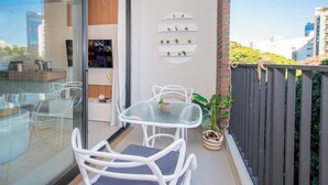 A balcony with a glass table and chairs, a potted plant, and a shelving unit with small plants. - Walk to Malls 200Mbps Pool, Gym & BBQ (Asunción)