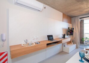Ein modernes Zimmer mit einem Holztisch, einem Laptop, einem Flachbildfernseher und einer kleinen Sitzecke.