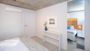 A modern bedroom with a bed, a bedside table, a bench, a framed picture, and a mirror reflecting a bed and a nightstand. - Walk to Malls 200Mbps Pool, Gym & BBQ (Asunción)