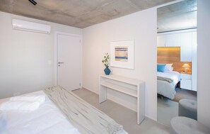 Ein modernes Schlafzimmer mit einem Bett, einem Nachttisch, einer Bank, einem gerahmten Bild und einem Spiegel, der ein Bett und einen Beistelltisch reflektiert.