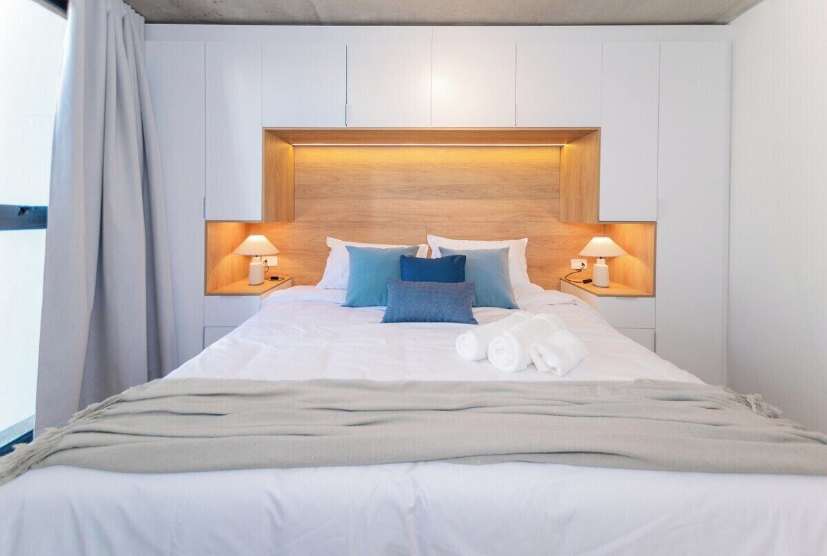 A neatly made bed with pillows, a blanket, and rolled towels.