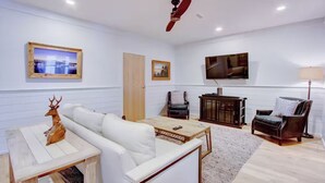 Un soggiorno con un divano bianco, un tavolino in legno, una TV a parete e una ventola a soffitto.