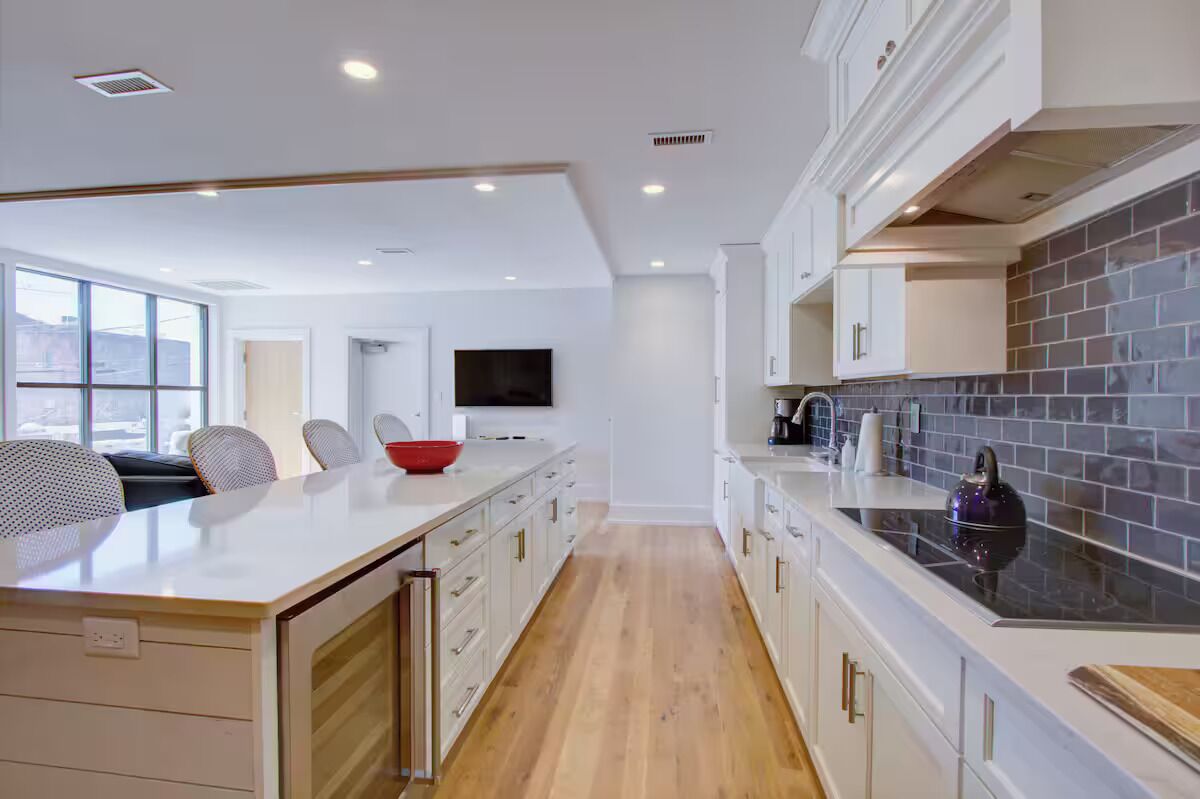 A modern kitchen with a central island, white cabinetry, and a tiled backsplash.