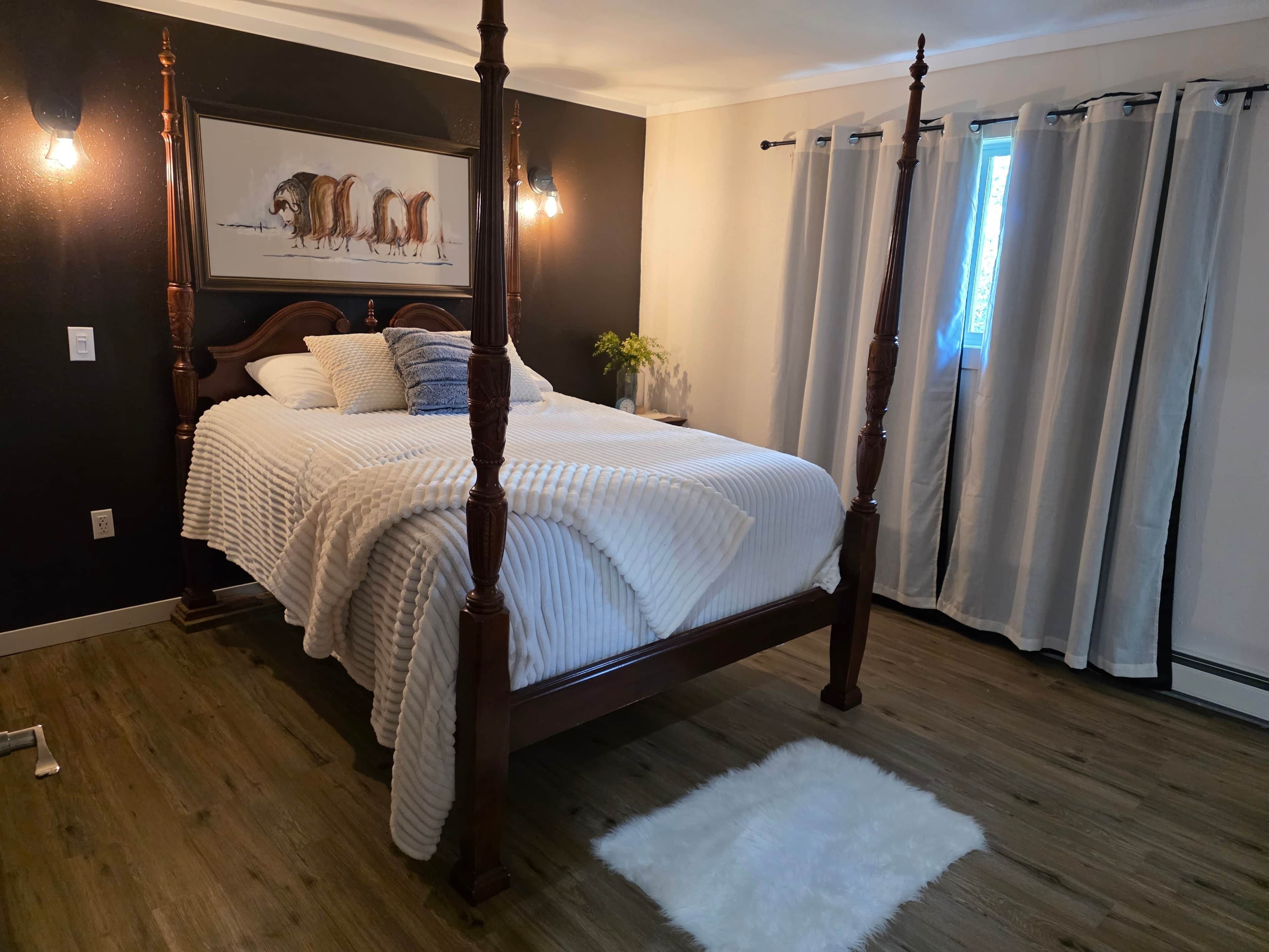 Un lit à baldaquin avec une couvre-lit blanche à texture, un plancher en bois foncé et un tapis blanc.