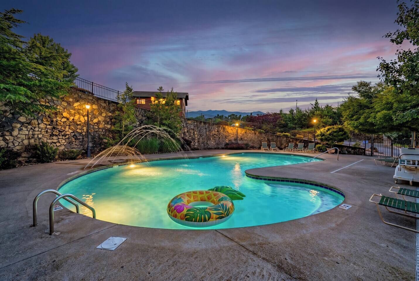A swimming pool with a water fountain, lounge chairs, and a stone wall.