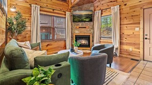 A cozy cabin interior with wooden walls, a fireplace, a sofa, and a chair. - Killer View|Amazing Pool|2 mi Gburg|Game Rm|Modern (Gatlinburg)