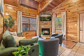 A cozy cabin interior with wooden walls, a fireplace, a sofa, and a chair. - Killer View|Amazing Pool|2 mi Gburg|Game Rm|Modern (Gatlinburg)