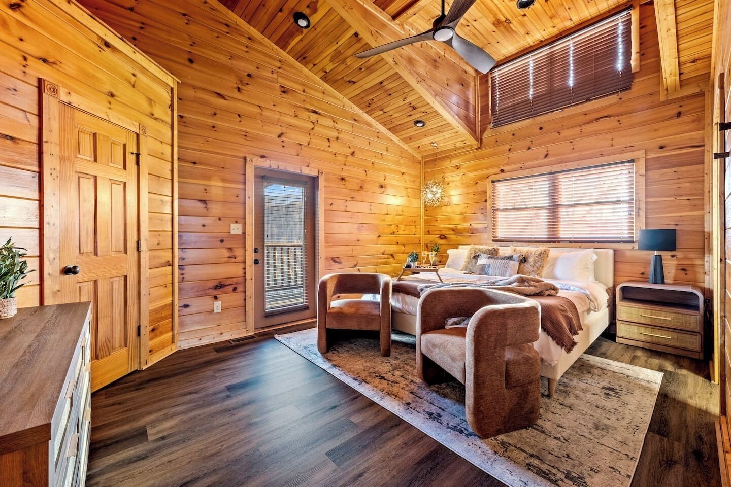 A log cabin bedroom with a bed, two chairs, a nightstand, and a ceiling fan.
