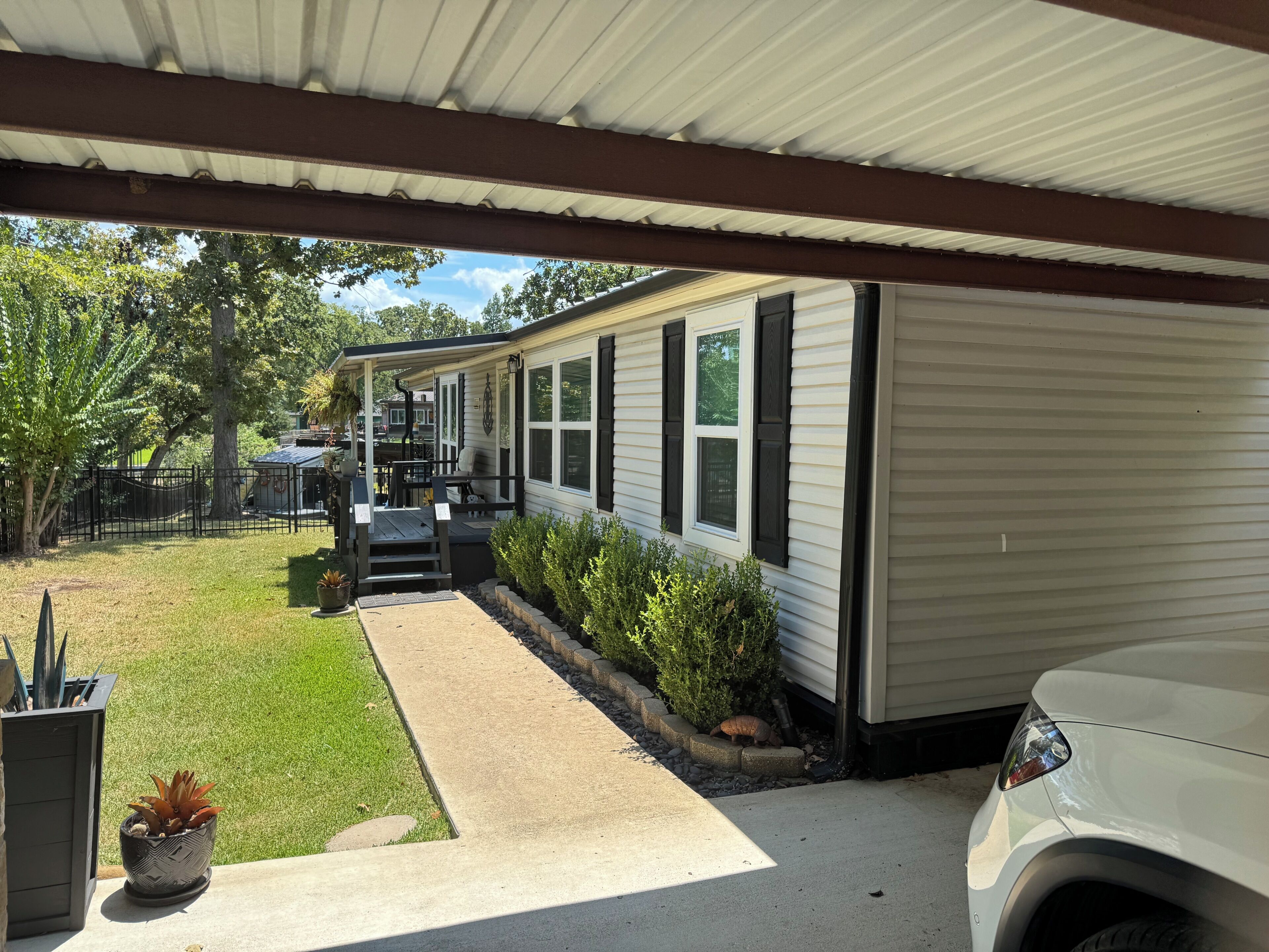 A covered porch with a concrete pathway leading to a white mobile home with black shutters.