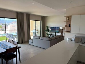 A modern living room with a sofa, a dining table with chairs, a TV, and a view of a pool and mountains. - New Luxury Apartment - Terrazas San Carlos (San Carlos)