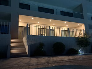 Ein modernes Gebäude mit Balkon, Stufen zum Eingang und einer gut beleuchteten Fassade.