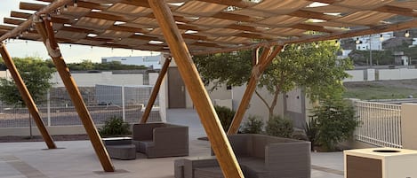 A wooden pergola with light fixtures, outdoor seating, and a branded trash bin.