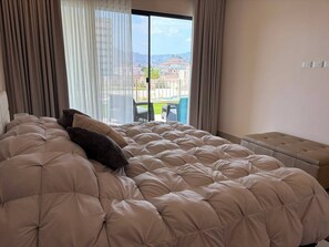 A bedroom with a large bed, a bench, and a view of a pool and buildings. - New Luxury Apartment - Terrazas San Carlos (San Carlos)