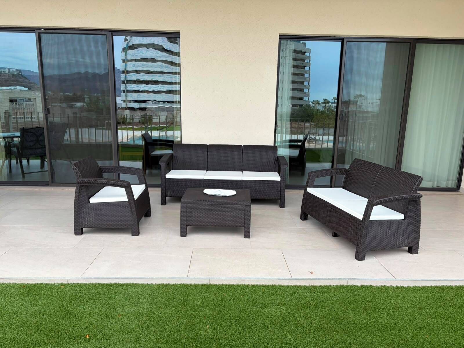 Een terras buiten met rieten meubels, waaronder een bank, twee fauteuils en een salontafel.