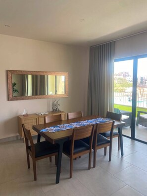 Een eetgedeelte met een tafel gedekt voor vier personen, een houten kast, een grote spiegel en uitzicht door een glazen deur.