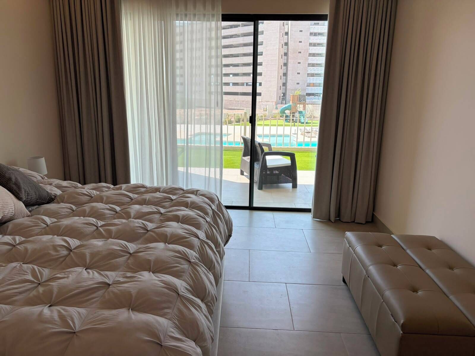 Habitación de hotel con una cama grande, un sofá y vistas a una piscina y edificios.