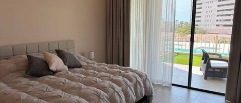 A bedroom with a large bed, a nightstand, a lamp, and a view of a swimming pool through a glass door.