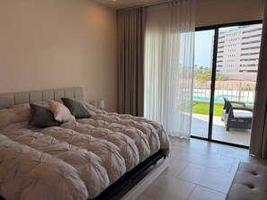 A bedroom with a large bed, a nightstand, a lamp, and a view of a swimming pool through a glass door. - New Luxury Apartment - Terrazas San Carlos (San Carlos)