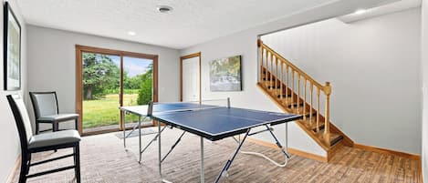 Une pièce avec une table de ping-pong, deux chaises, un escalier et une porte donnant sur l’extérieur.