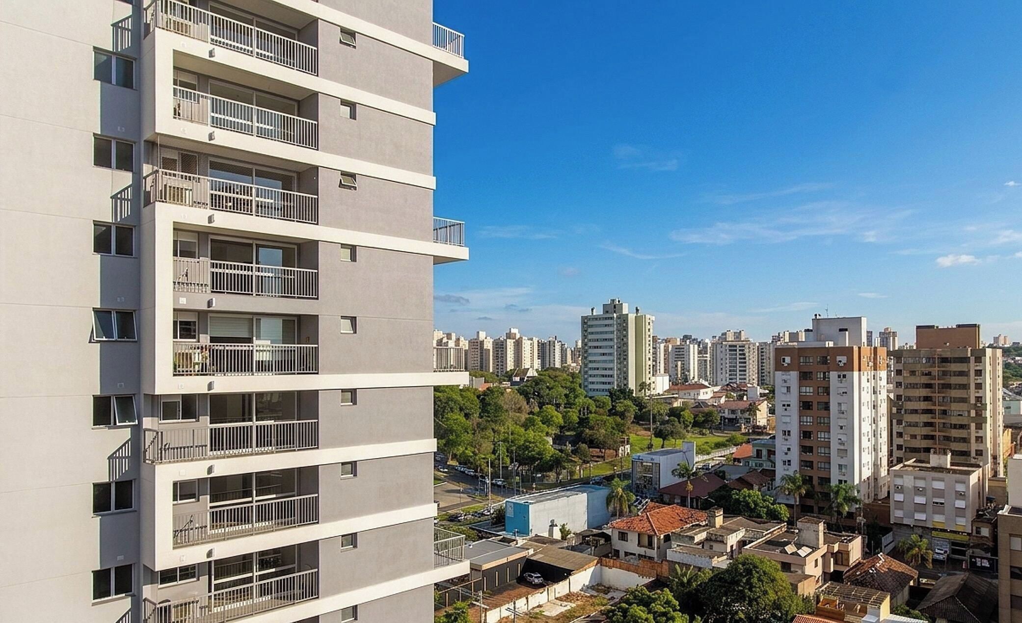 Edifício residencial com vários andares e varandas, cercado por outros edifícios altos e uma combinação de áreas verdes e construções urbanas.