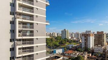 Edifício residencial com vários andares e varandas, cercado por outros edifícios altos e uma combinação de áreas verdes e construções urbanas.
