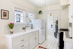 A kitchen with white cabinets, a white refrigerator, a sink, and a window with a view of trees. - Cozy 1-bedroom apartment in beautiful Venice Beach with AC (Los Angeles)