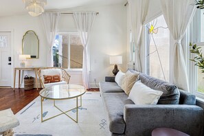 Een moderne woonkamer met een grijze bank, een glazen salontafel en een rieten fauteuil.