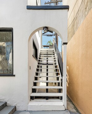 A staircase leading to a second-floor entrance, flanked by white walls and a wooden handrail. - Cozy 1-bedroom apartment in beautiful Venice Beach with AC (Los Angeles)