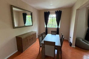 Ein Essbereich mit Tisch, Stühlen, einem Holzschrank und einem Spiegel an der Wand.