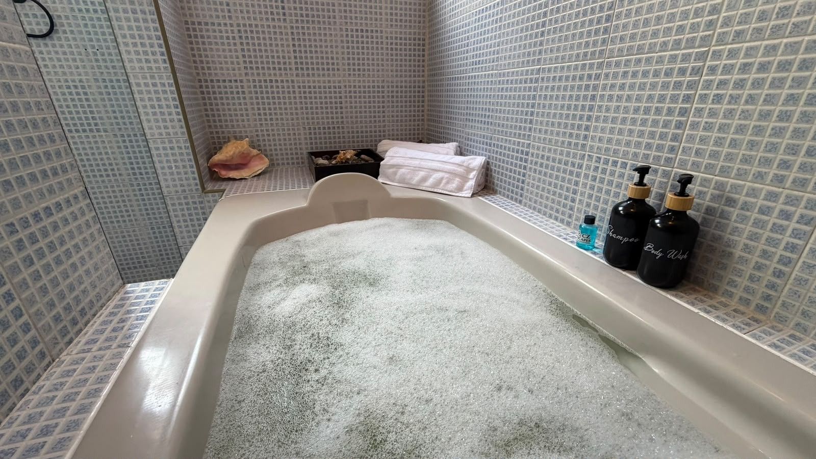Une baignoire remplie d’eau, une serviette, une petite boîte et deux bouteilles de shampoing et de gel douche.