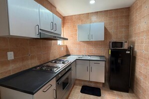A compact kitchen with a gas stove, oven, microwave, and a sink. - Amplio Oasis con Balcón en Roma Norte (Mexico City)
