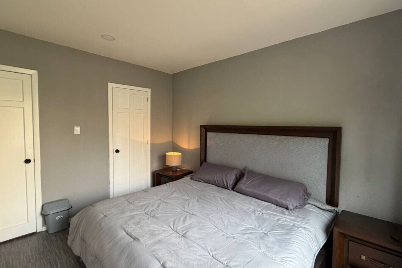 A bedroom with a bed, a nightstand, a lamp, and a door.