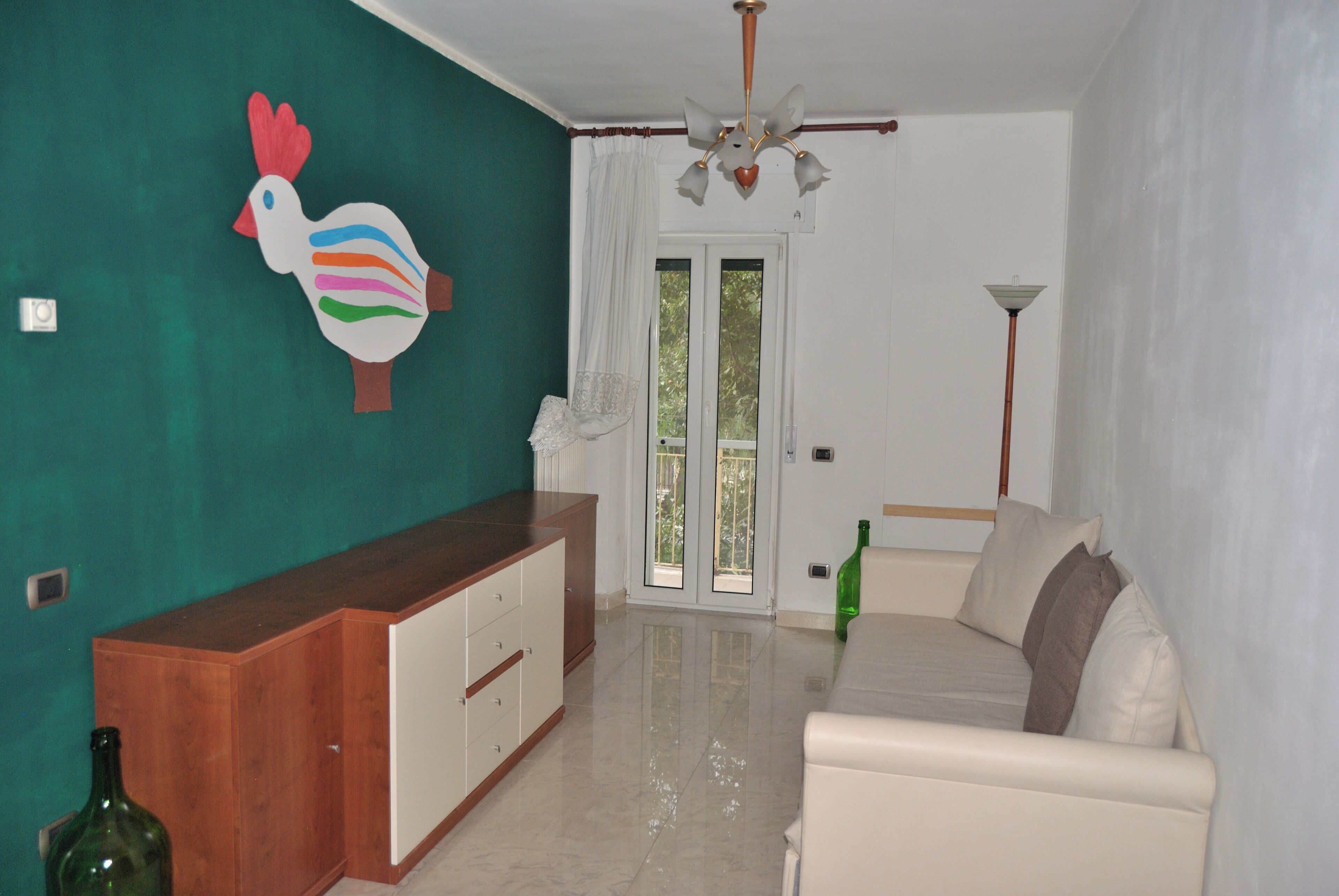 A living room with a sofa, a wooden cabinet, a ceiling fan, and a green bottle.