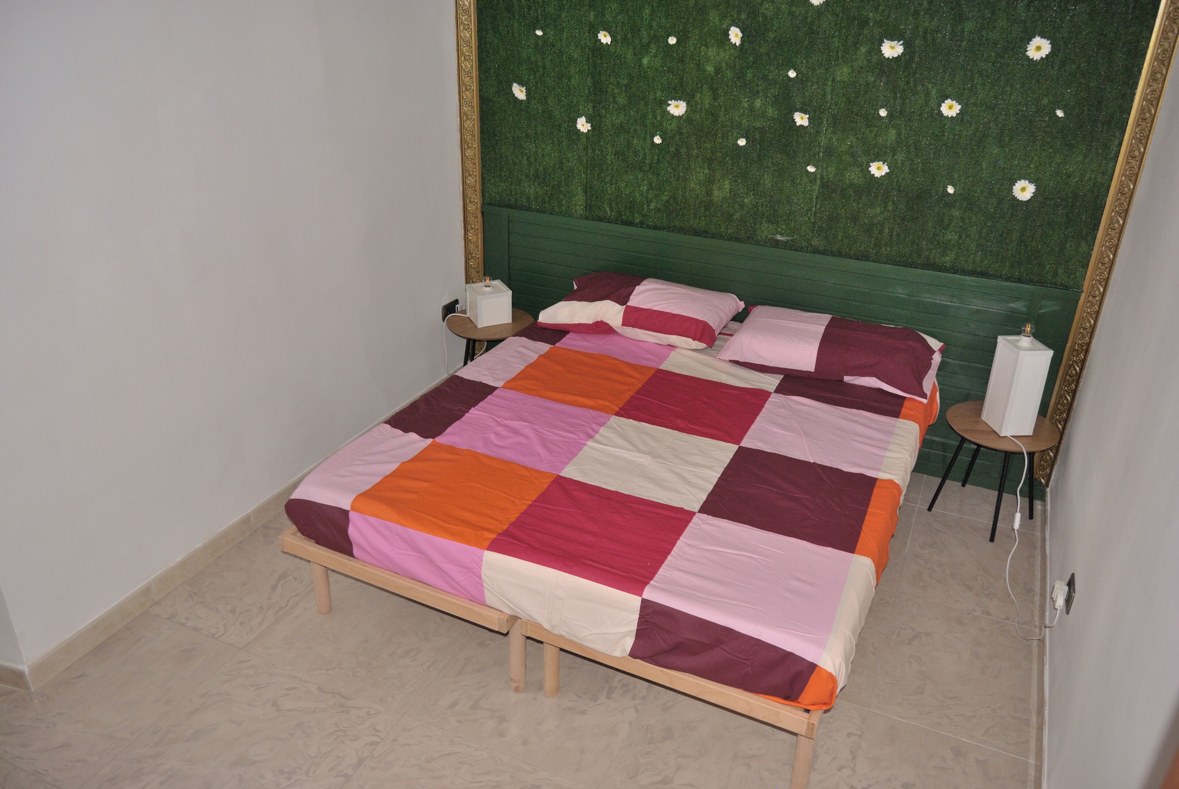 A bed with a multicolored quilt, a green headboard, and a nightstand with a lamp.