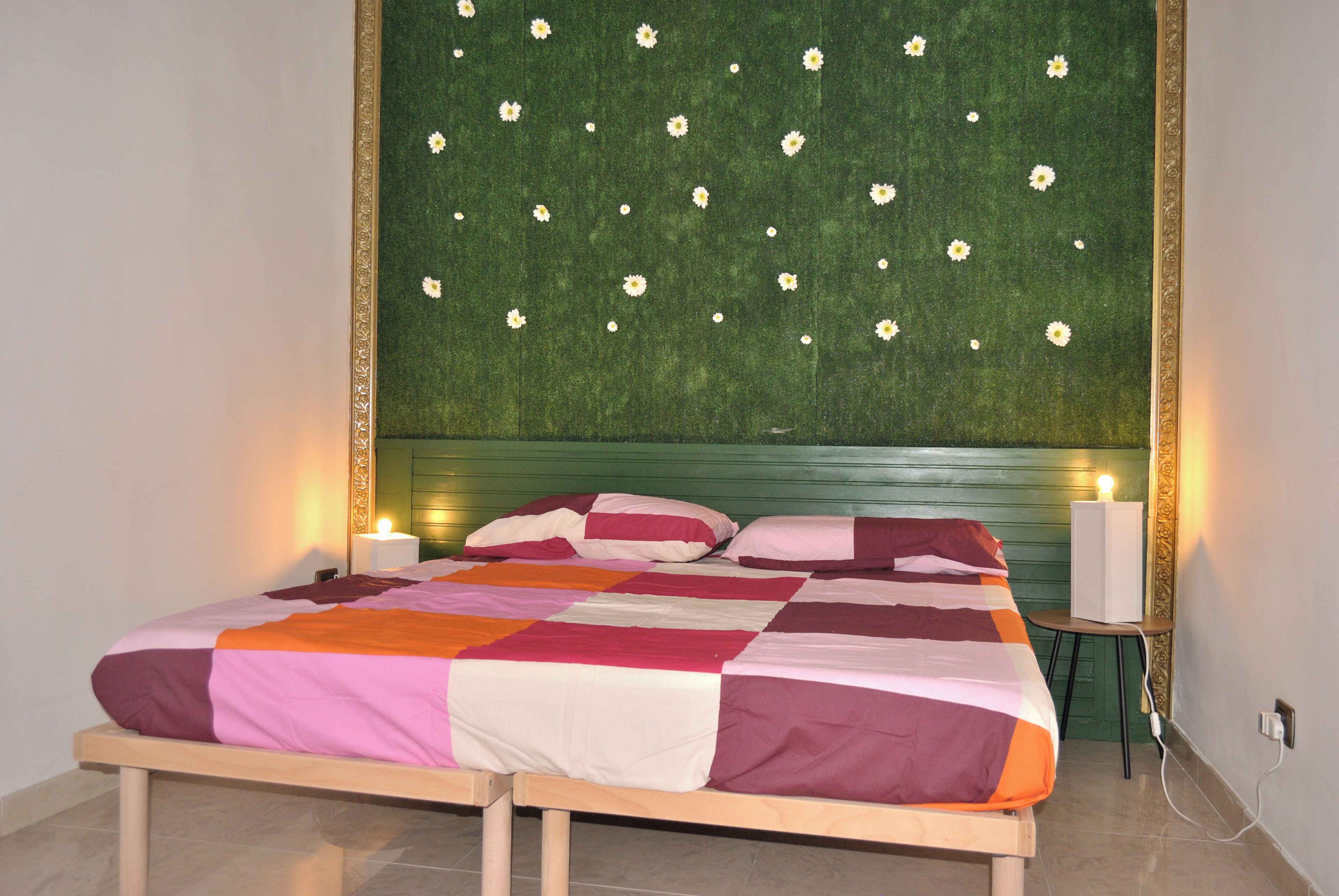 Uma cama com cabeceira verde, duas luminárias de cabeceira e um cobreleite estampado.
