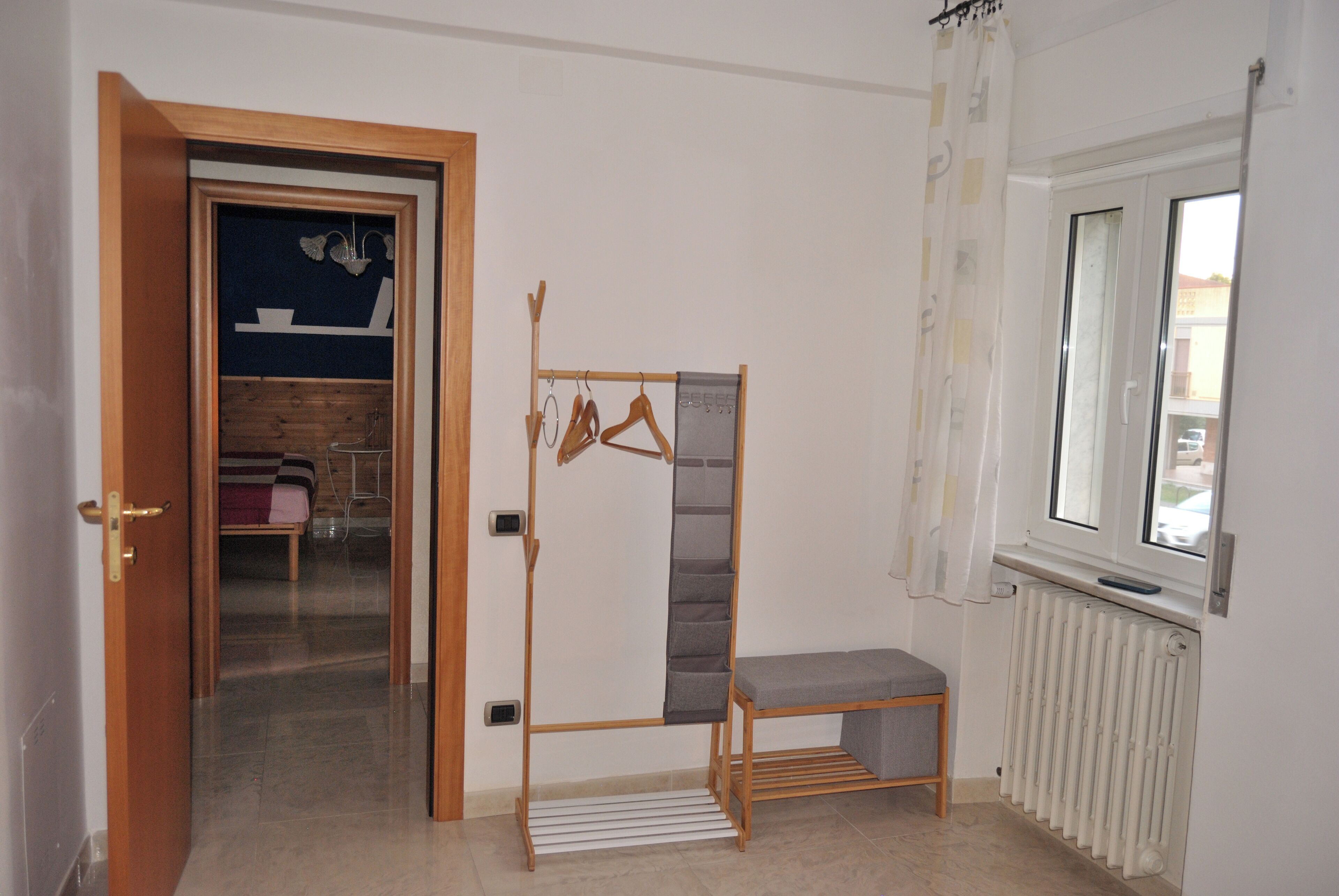A room with a wooden wardrobe, a bench, a radiator, and a window with curtains.