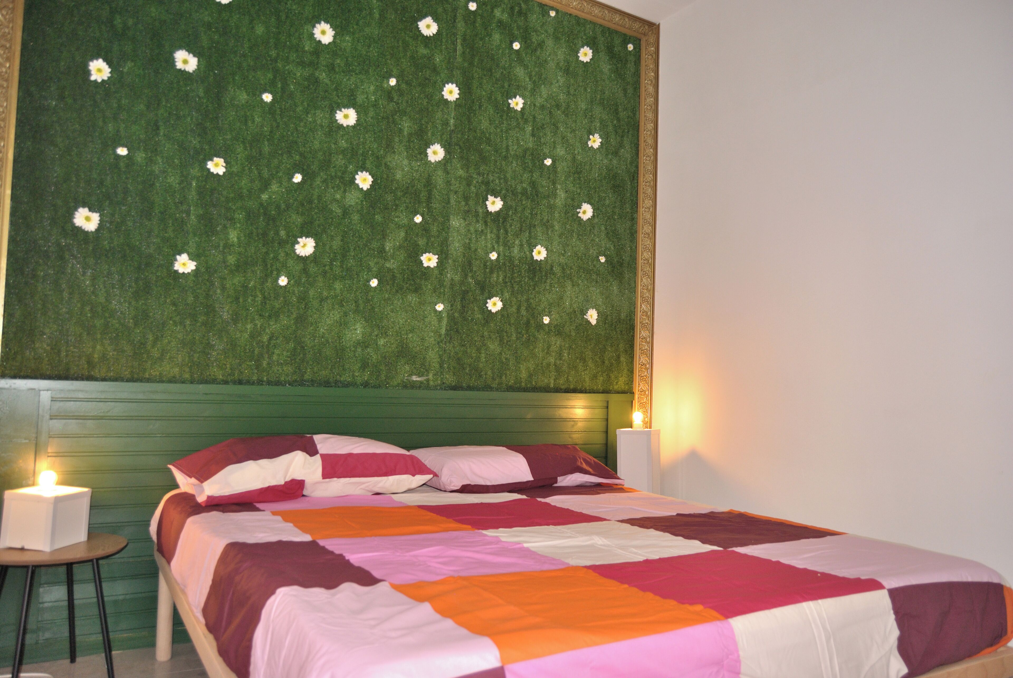 Una camera da letto con una testiera verde, un letto con una coperta multicolore, due abat-jour e un piccolo tavolo.