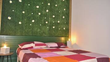 Una camera da letto con una testiera verde, un letto con una coperta multicolore, due abat-jour e un piccolo tavolo.