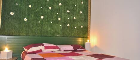 A bedroom with a green headboard, a bed with a multicolored quilt, two bedside lamps, and a small table.