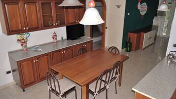 Une cuisine avec des meubles de rangement en bois, une table à manger avec des chaises, un téléviseur et un élément décoratif mural.