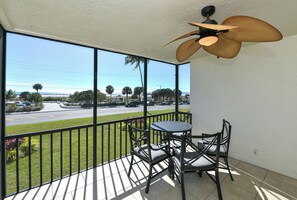 Ein Balkon mit Tisch und Stühlen, einem Deckenventilator und Blick auf eine Straße und den Strand.