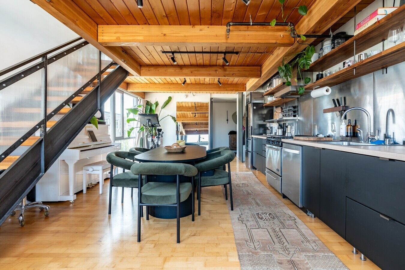 A modern kitchen with stainless steel appliances, a wooden ceiling, and a dining area with a round table and chairs.