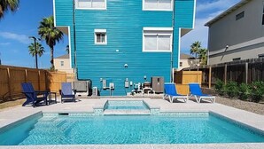 Uma piscina com espreguiçadeiras e um prédio azul ao fundo.