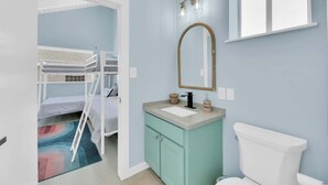 Quarto com beliches, banheiro com pia, espelho e vaso sanitário.