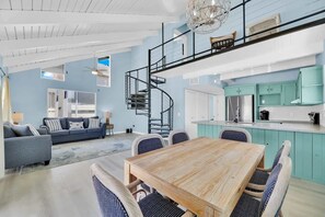 A spacious living area with a dining table, sofa, and a spiral staircase leading to an upper level. - Isla Bella - 3BR, Private Pool, Near SP Beach (South Padre Island)