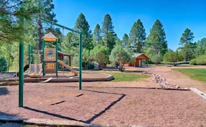 A playground with a slide and climbing structures, surrounded by trees and a gravel path. - NEW - The Cozy Bison (Show Low)
